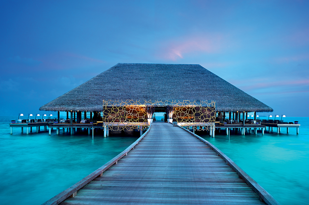 Elegantes Abendrestaurant über dem türkisblauen Wasser des Luxusresort Velaa Private Island Malediven bei Abenddämmerung