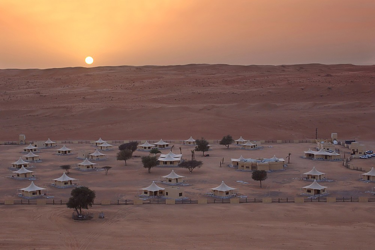 Wüstencamp aus weißen Zelten in mitten der wÜste des Omans bei Sonnenuntergang